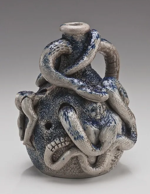 Grey stoneware jug entirely covered in modelled snakes coiling over its shoulder and around a grimacing face at the front