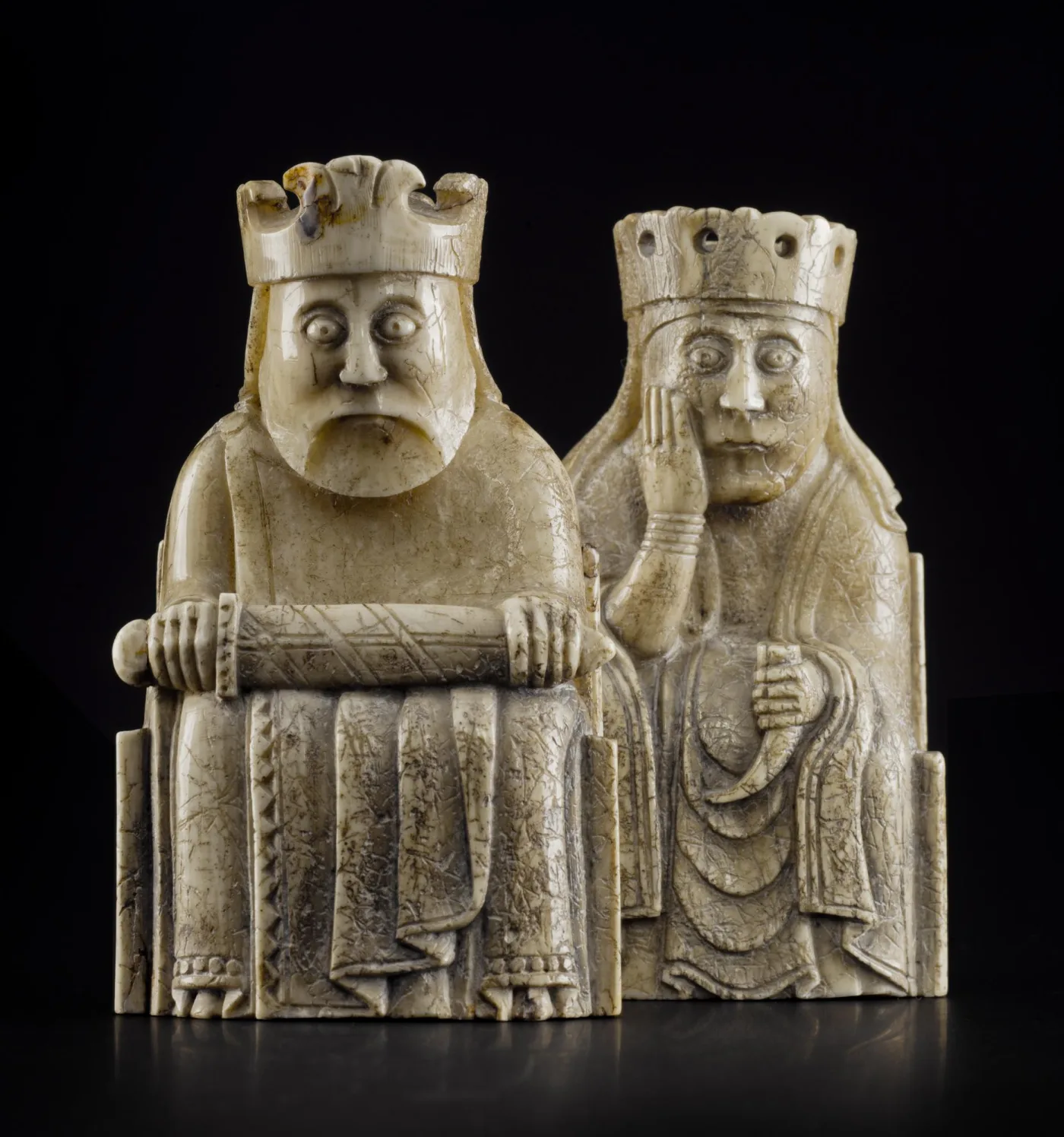 Two carved walrus ivory chess pieces, a king and a queen seated on high-backed thrones with solemn wide-eyed faces