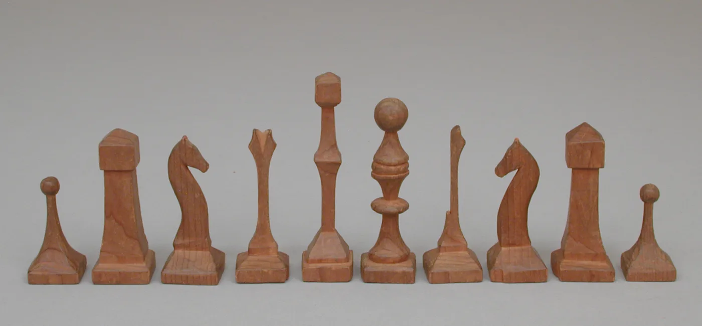 Ten hand-carved wooden chess pieces standing in a row on square bases, their surfaces cut into flat facets rather than turned