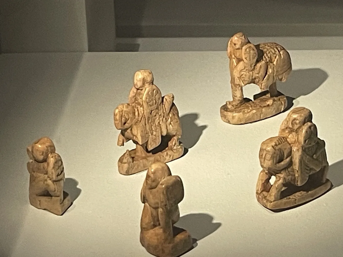 Five small worn ivory chess figures displayed on a pale ground, their carved details softened by age