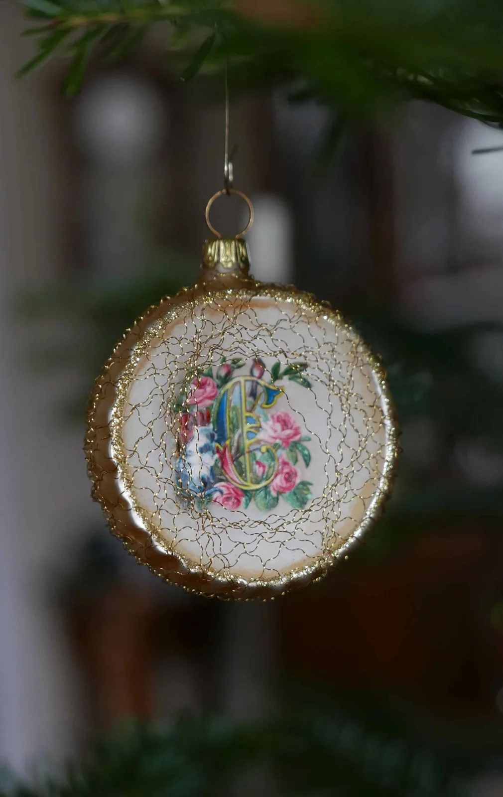 Flat disc-shaped ornament with a printed floral scrap at its centre, edged with gold tinsel and set in a crazed cream ground