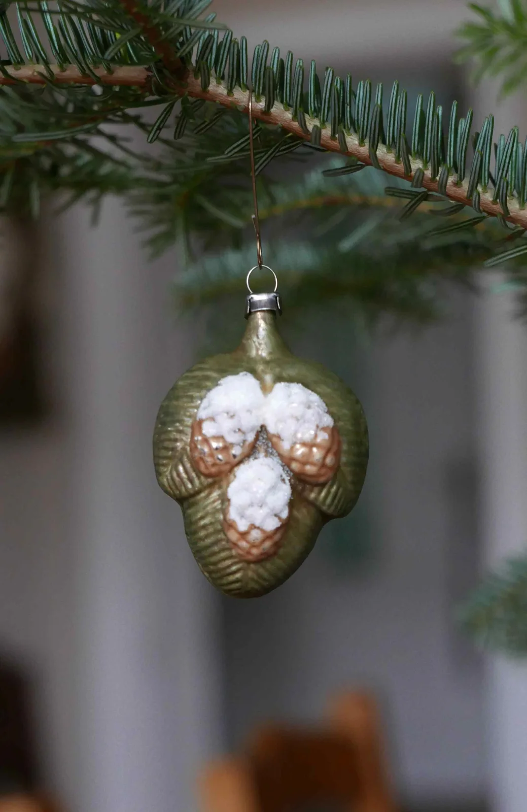 Glass ornament in the form of a green pine cone or berry cluster with three white frosted lobes, hanging from a branch