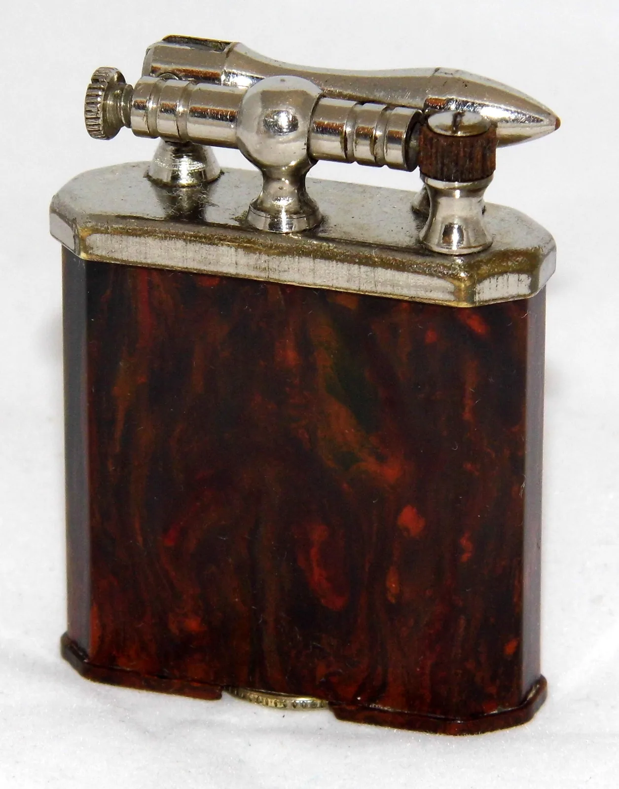Pocket lighter with a mottled red, brown and green marbled plastic body and a chromed horizontal arm mounted on three posts across the top, with a knurled screw at the left end and a bullet-shaped tip at the right