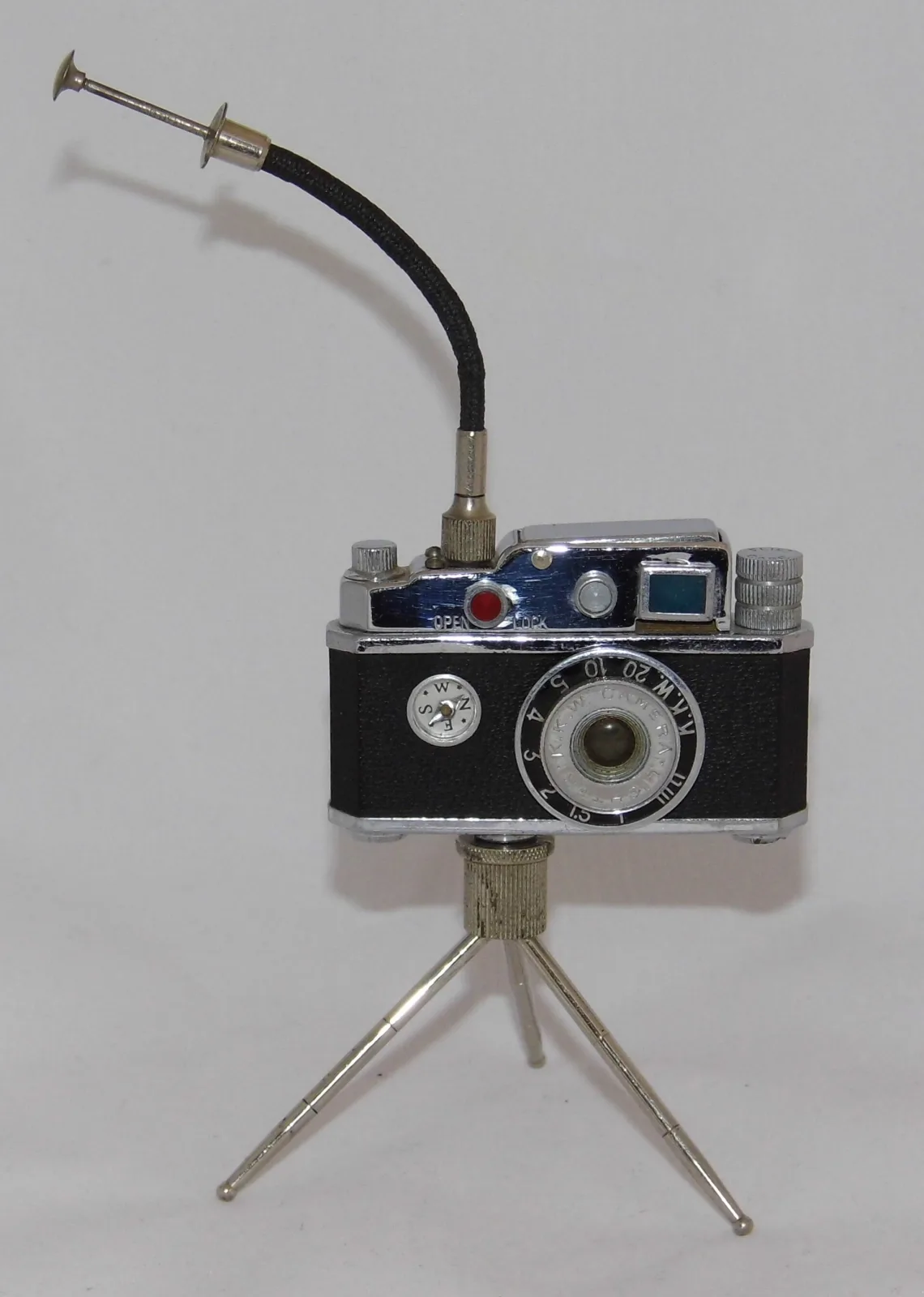 Miniature 35mm-camera-shaped lighter in black leatherette and chrome on a folding tripod, with a flexible gooseneck wand rising from the top plate and a compass set into the front