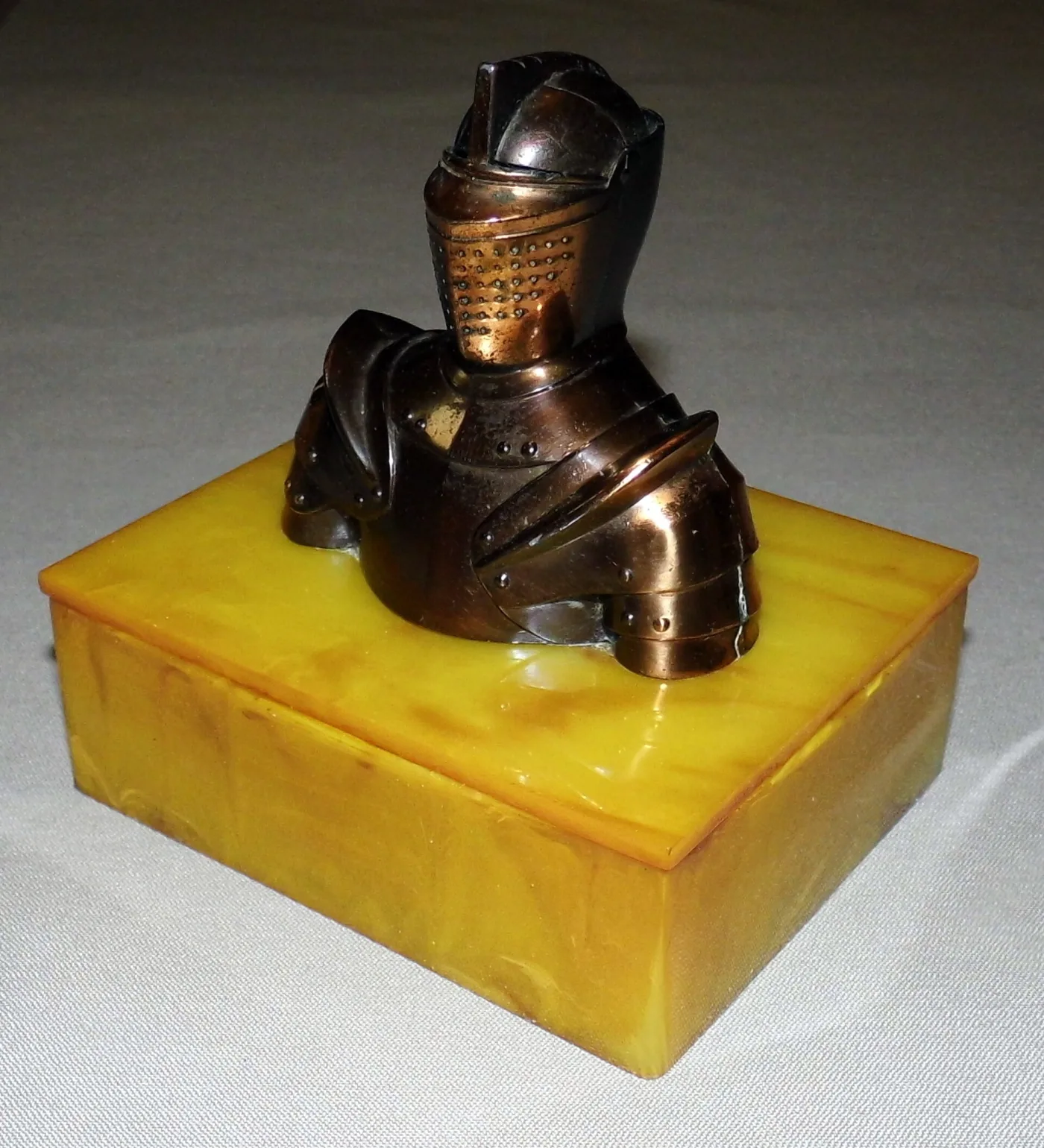 Copper-finished armoured knight's bust with a lifting visor, mounted on a marbled butterscotch-yellow plastic box