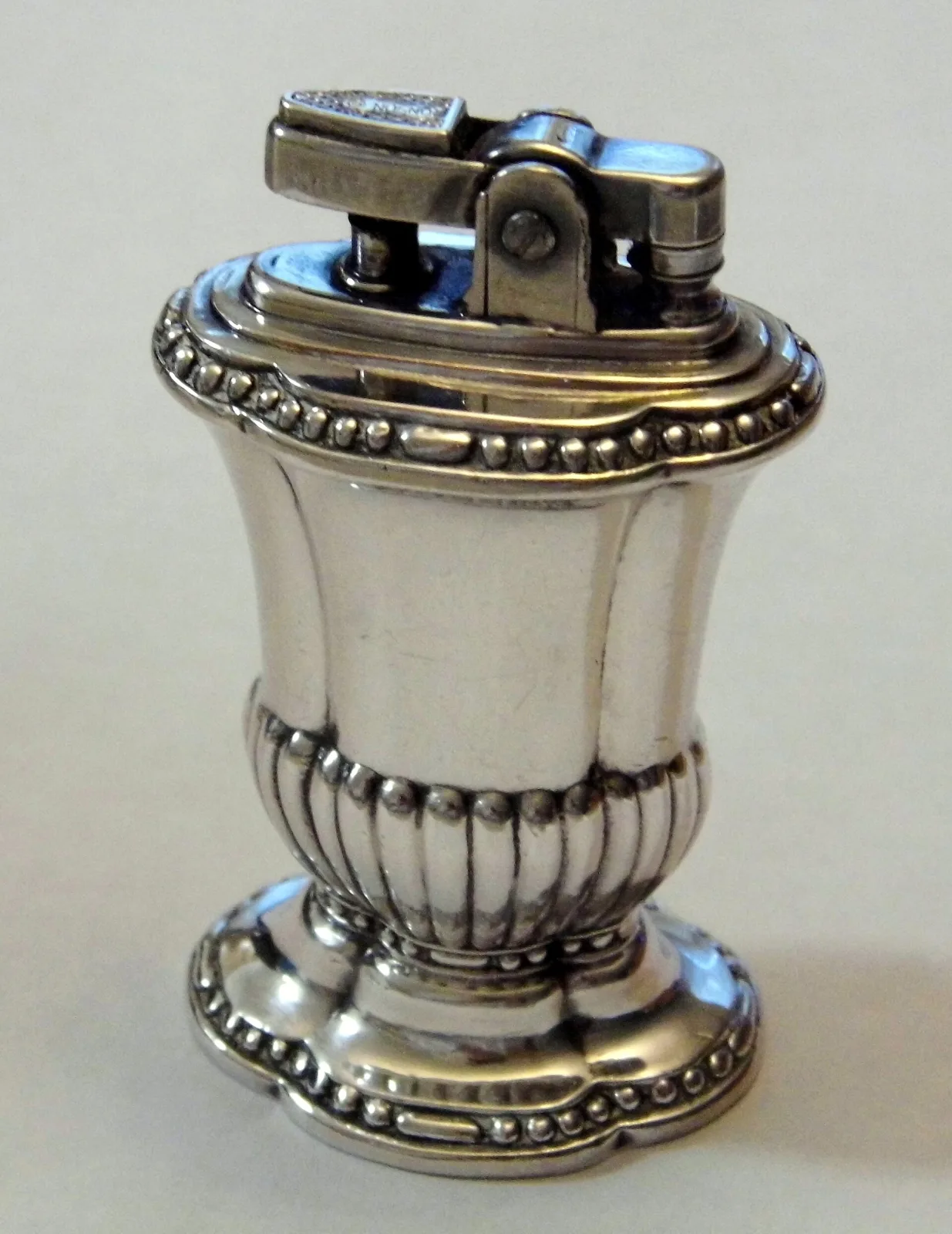 Silver-coloured table lighter in classical urn form with a beaded rim, gadrooned lower body and shaped oval foot, the high points of the beading rubbed to a warmer yellow metal