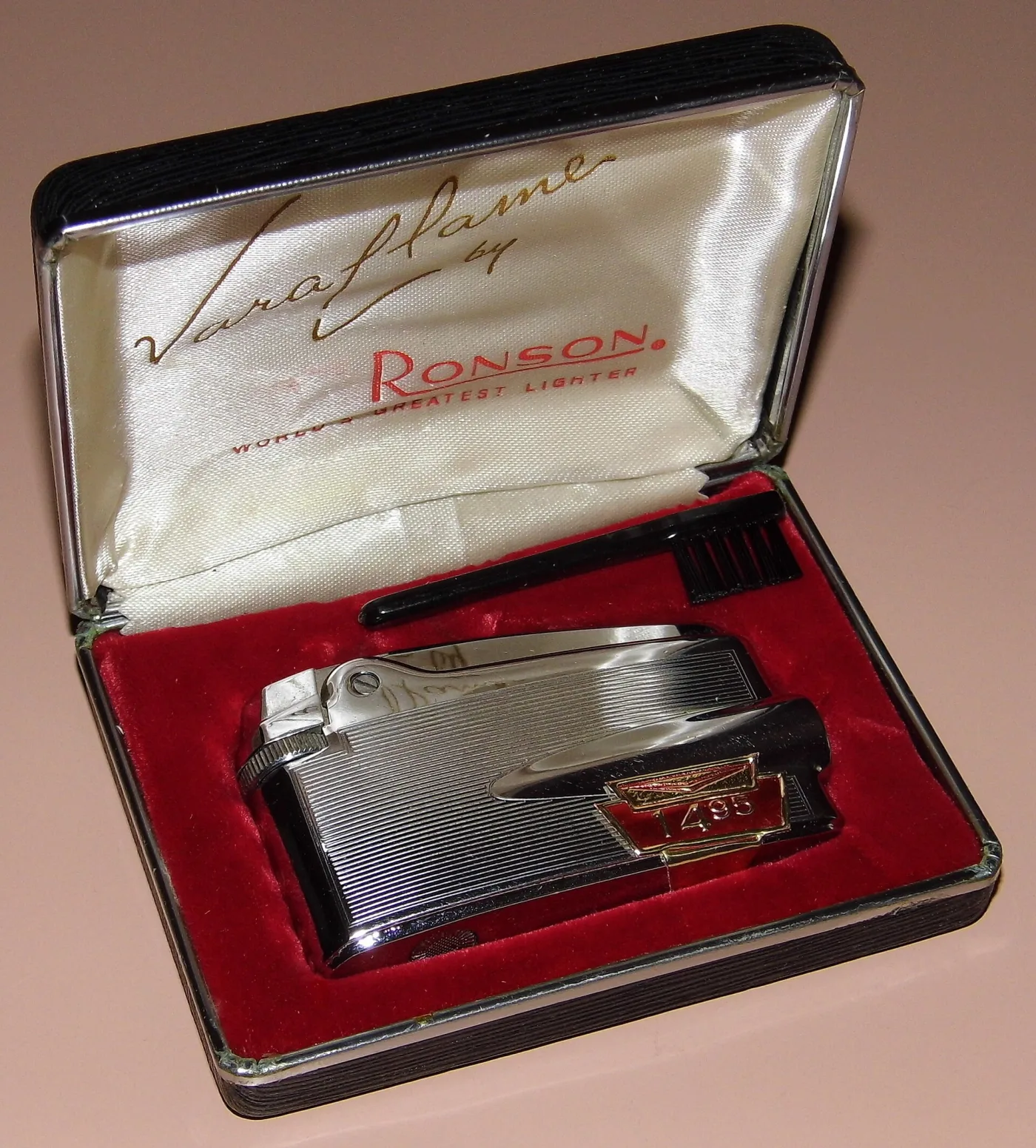 Chrome pocket lighter with engine-turned vertical lines in a leatherette case lined in red velvet, the lid printed Varaflame by Ronson, with a cleaning brush and a paper price tag reading 14.95
