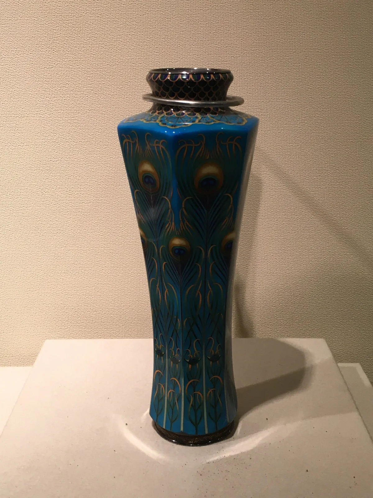A blue cloisonne vase covered with an overlapping peacock-feather pattern, shown in a museum case