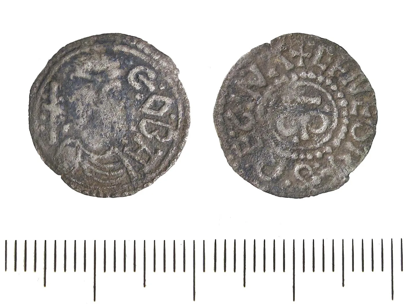 Two faces of a small early medieval silver penny against a millimetre scale, both sides carrying legends in Latin capitals around a central design