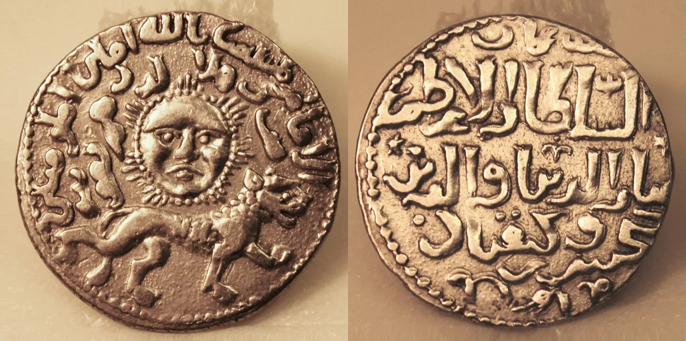 Two faces of a silver coin: on the left a lion walking left beneath a human-faced sun disc, on the right four lines of Arabic script in a circular border
