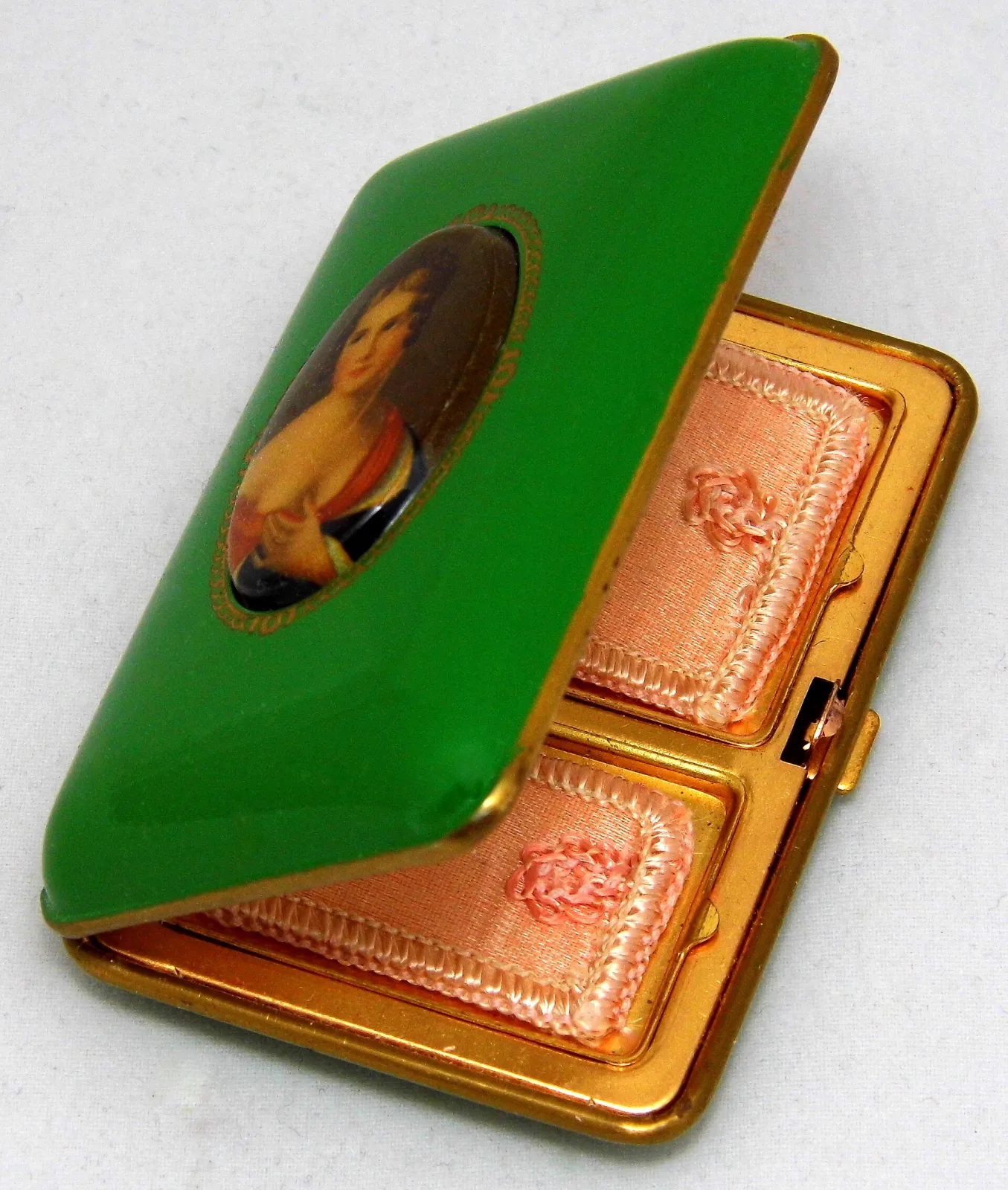 Small rectangular compact standing open, its lid faced in bright green enamel with an oval painted portrait of a woman, the base divided into two square wells lined with pink satin puffs, in a gilt-metal frame with a side clasp