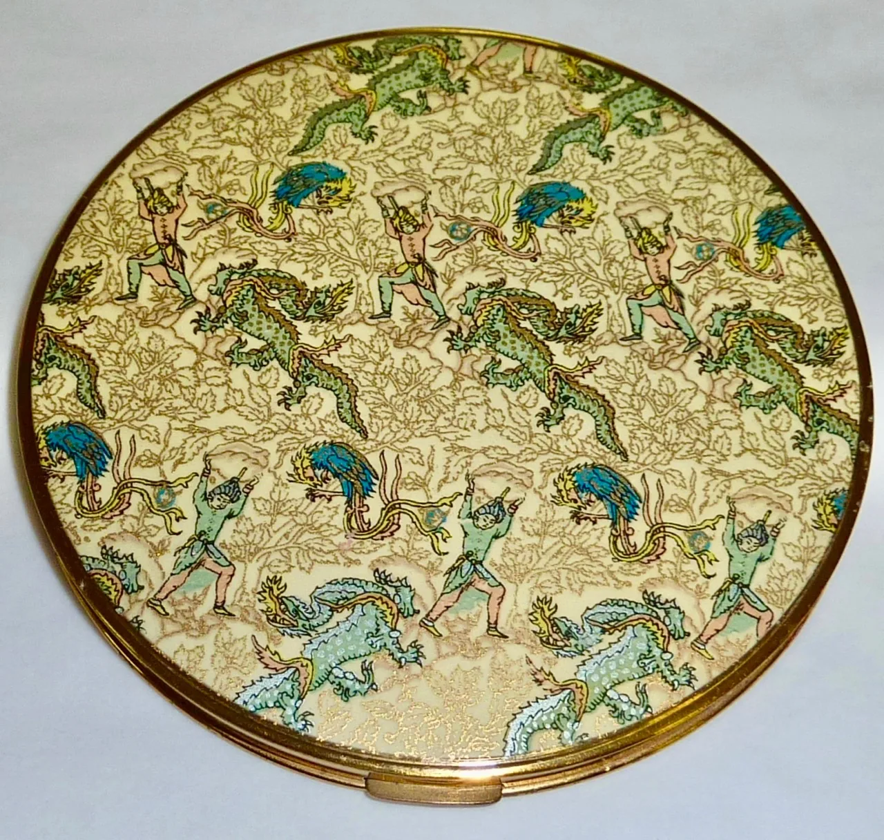 Round compact lid covered edge to edge in a small repeating pattern of pale green and blue dragons and figures on a gold-flecked ground