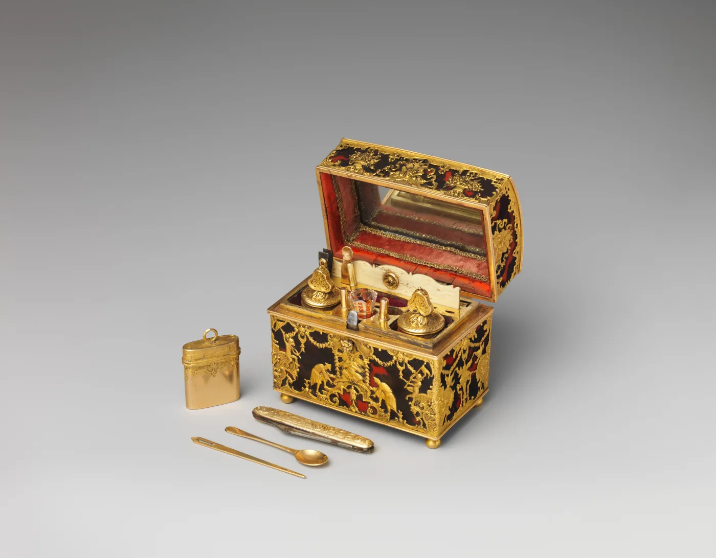 Small casket veneered in dark tortoiseshell inlaid with gold, standing open to show fitted bottles and covered boxes in a lined interior, with a folding knife, a pair of tweezers, a spatula and a small gold case laid out in front of it