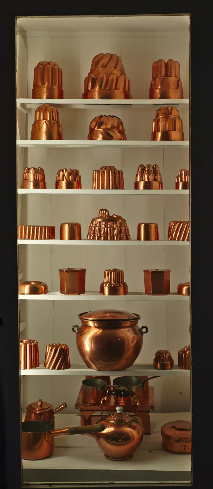 Tall glazed cabinet of seven shelves filled with copper jelly moulds of many shapes and sizes, with a large lidded stockpot and further copper vessels on the lower shelves
