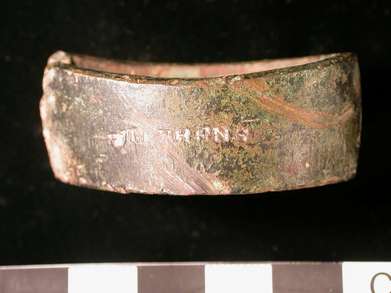 Side view of a small cast copper-alloy confectionery mould photographed against a black-and-white scale, its worn and corroded outer wall stamped with the name STEPHENS