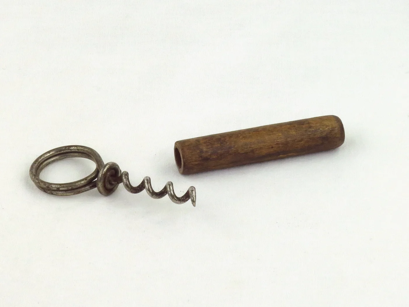 Small corkscrew with a ring-topped worm lying beside a plain turned wooden barrel that serves as both its sheath and its handle