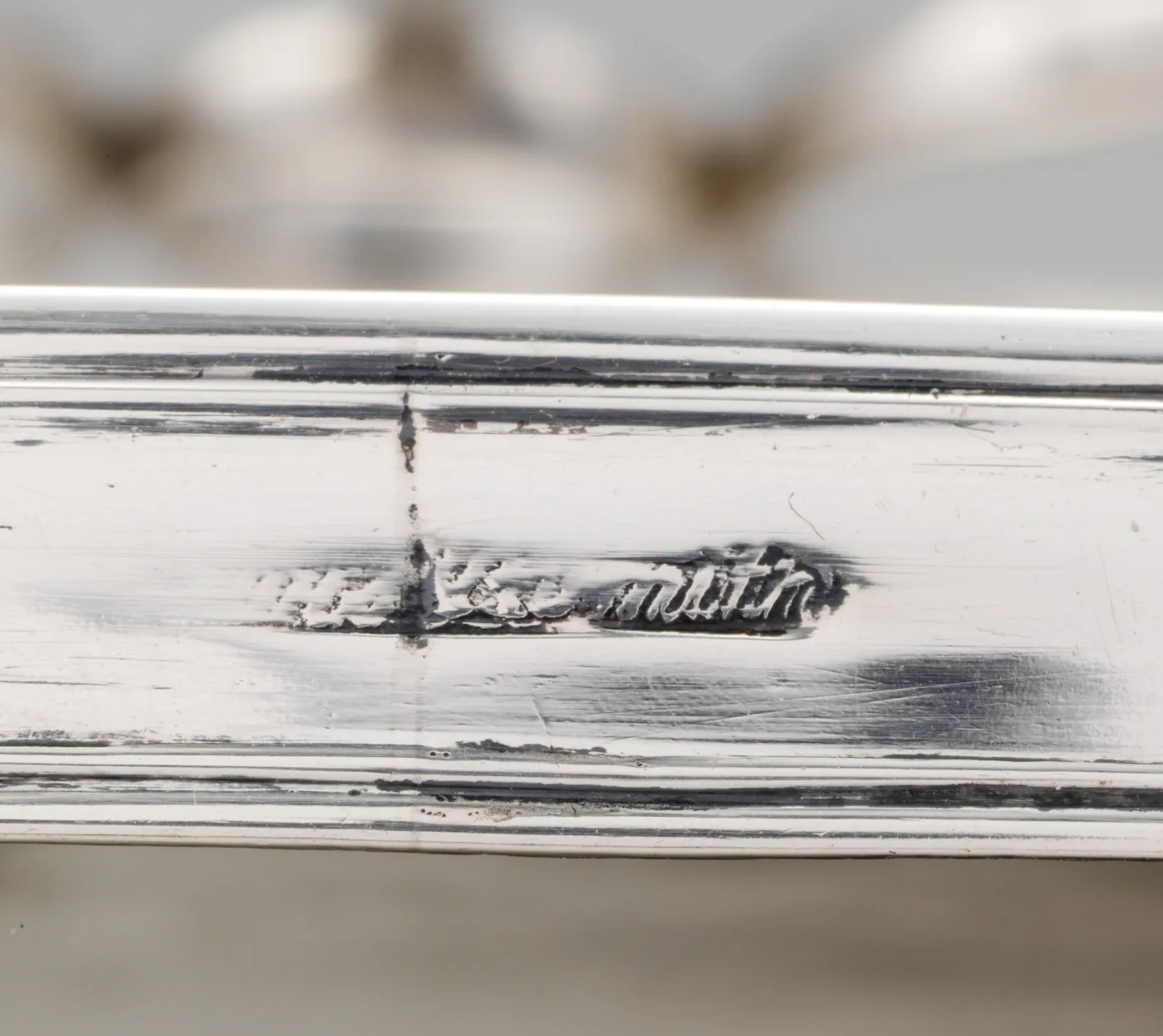 Close-up of the moulded rim of a silver cruet stand carrying a worn and partly illegible struck script mark whose final letters read m-i-t-h