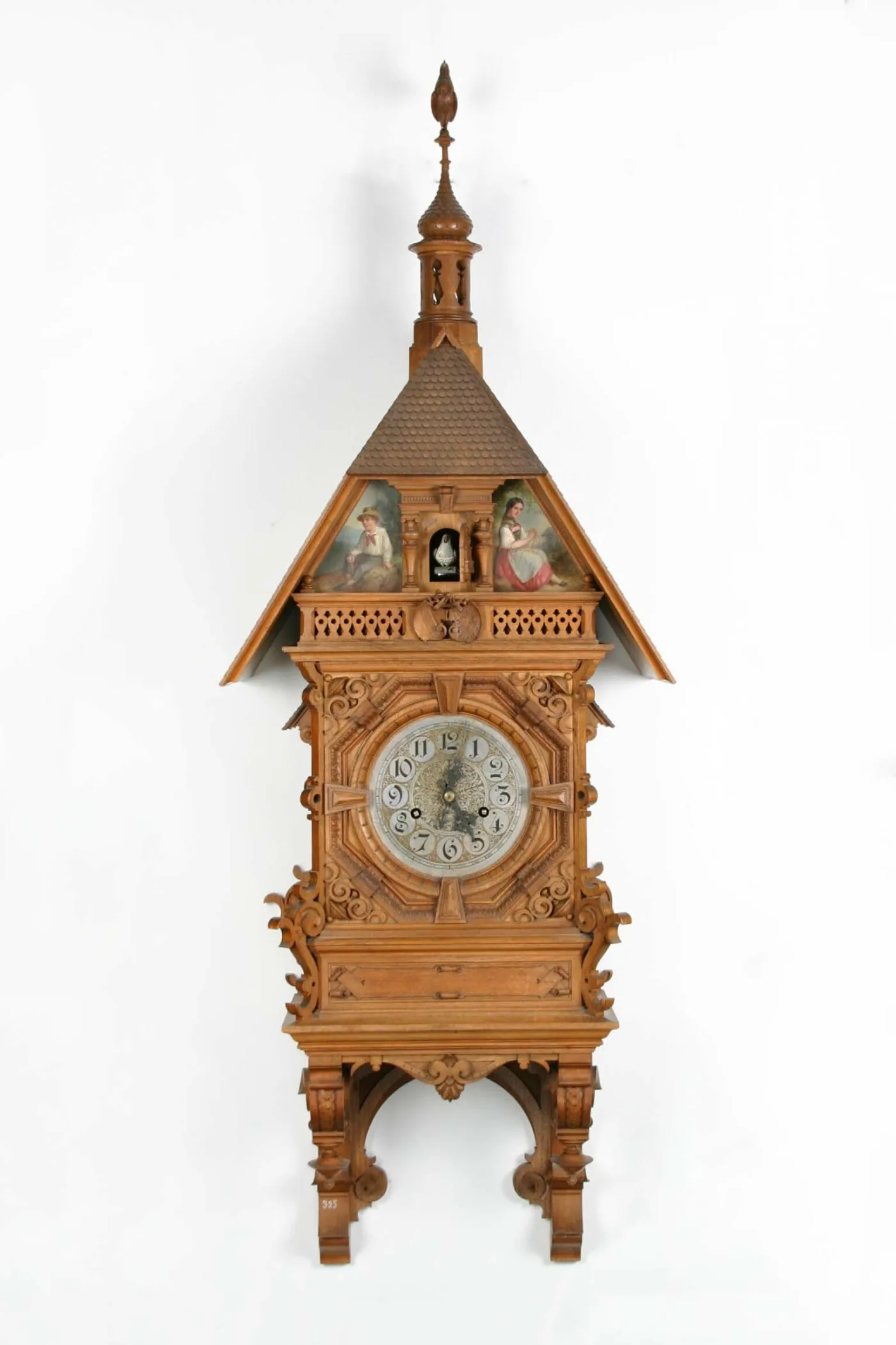 Tall tower-shaped cuckoo clock with a shingled spire, fretwork gallery, painted figure panels either side of the cuckoo niche and a silvered dial with Arabic numerals