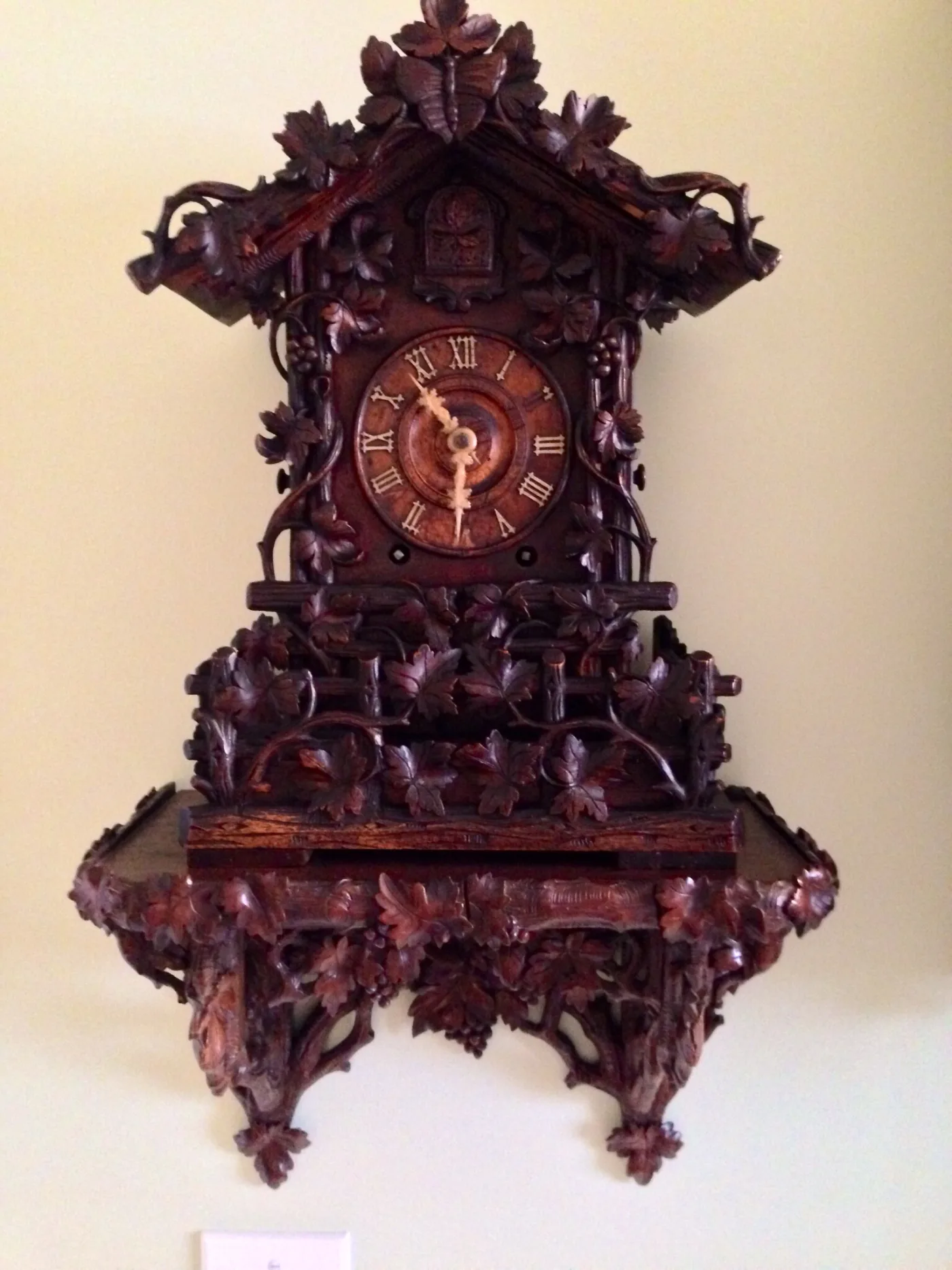 Dark carved Black Forest cuckoo clock with vine and maple-leaf carving, mounted on its matching carved wall bracket