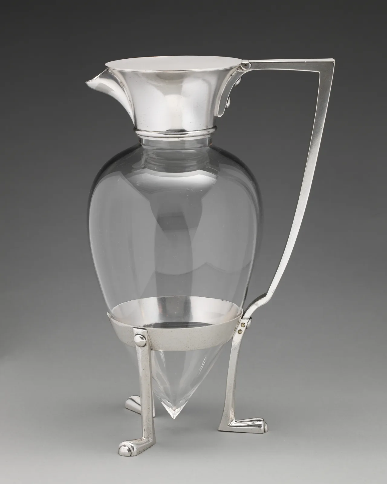 Plain conical glass jug body held in a silver-plate mount with a wide spouted collar, a straight angular handle set at right angles and three splayed legs ending in scrolled feet
