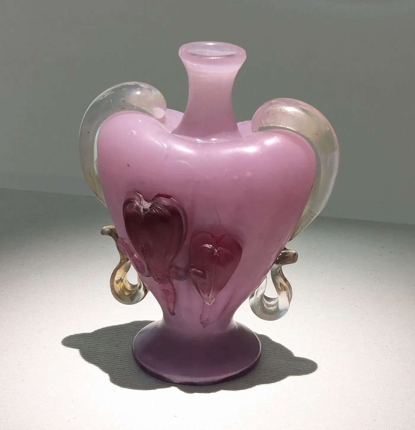 Tall glass vase with a pale pink body shading to purple, two applied looping clear handles at the shoulder and a softly mottled surface