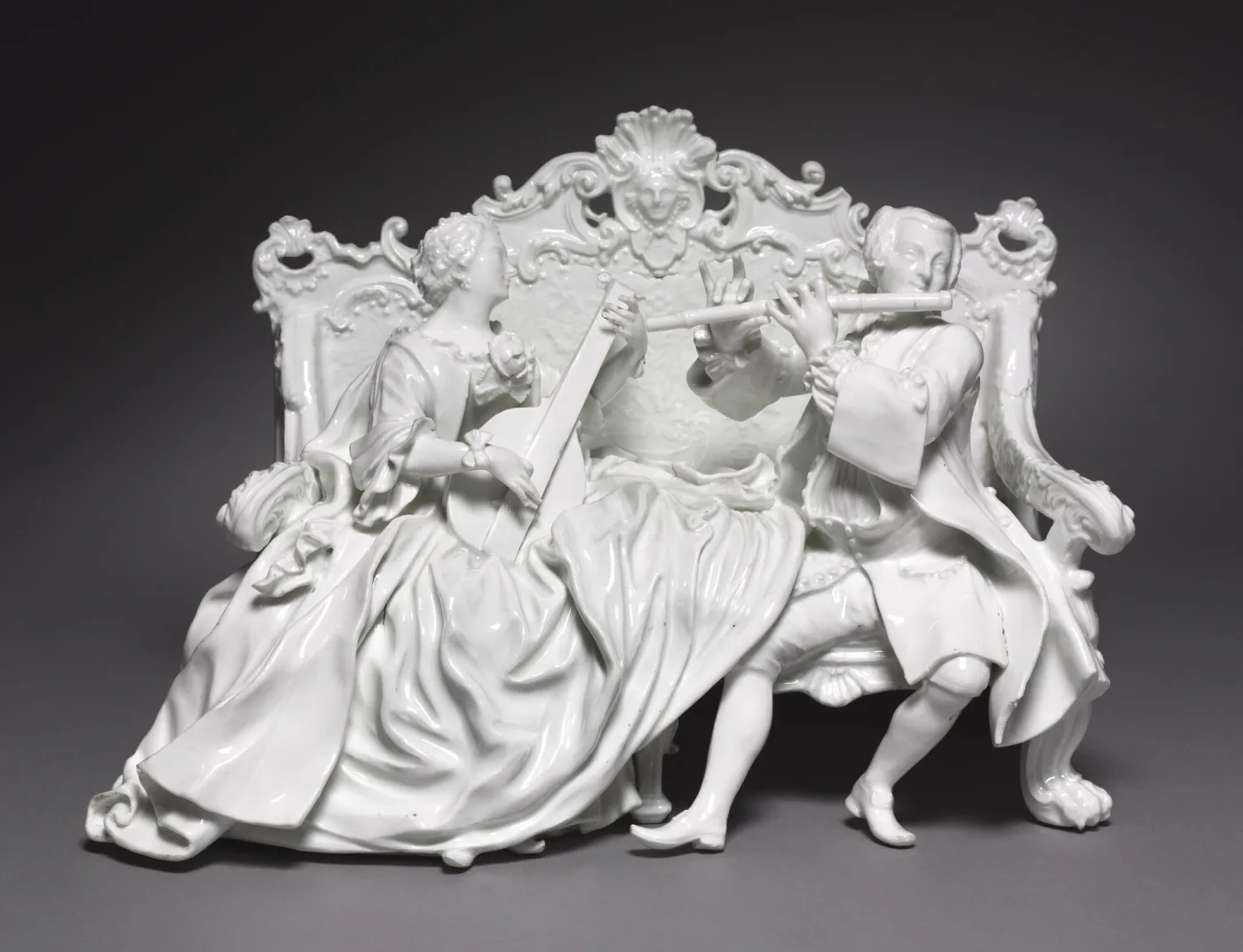 Group of white unglazed porcelain figures seated and standing around a scrolled base, several holding musical instruments, the whole undecorated so that only the modelling carries the design