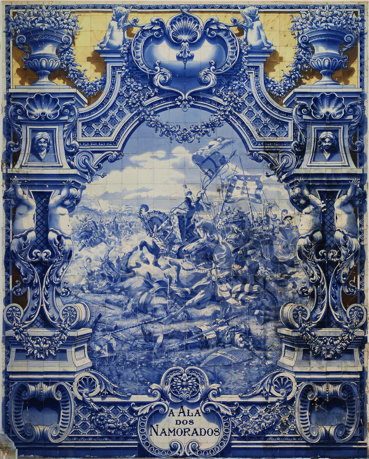 Large blue-and-white tile panel in an elaborate painted architectural frame with urns, putti and masks against a yellow ground, enclosing a crowded medieval battle scene with banners and lances