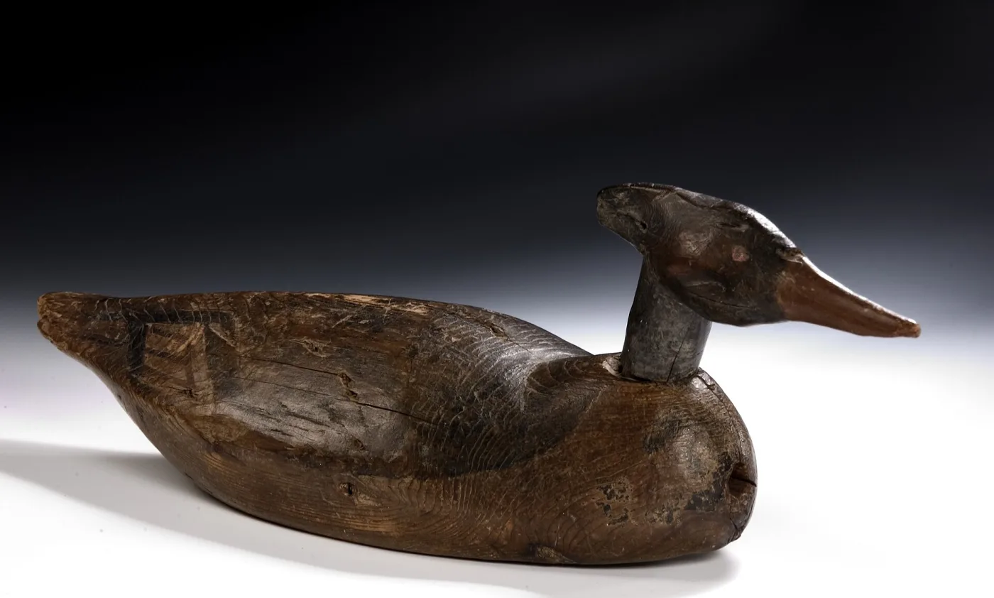Stripped merganser decoy in bare weathered wood, the head sitting on a cylindrical neck stump where it meets the body