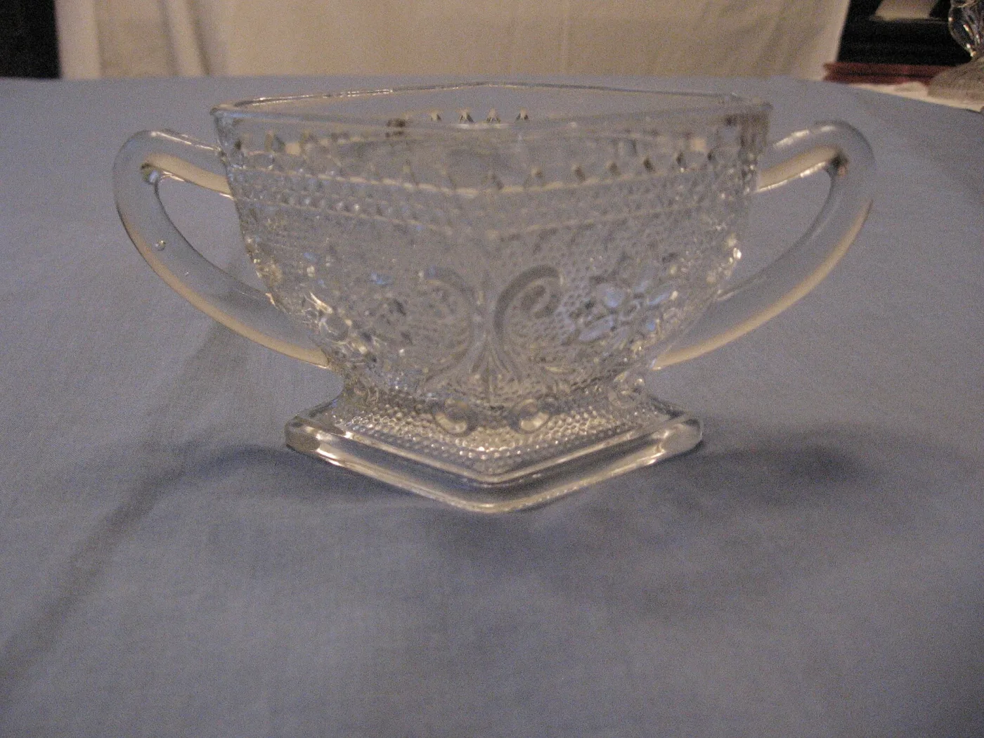Clear pressed glass two-handled sugar bowl on a square foot, with a dense stippled ground and scrolled panels