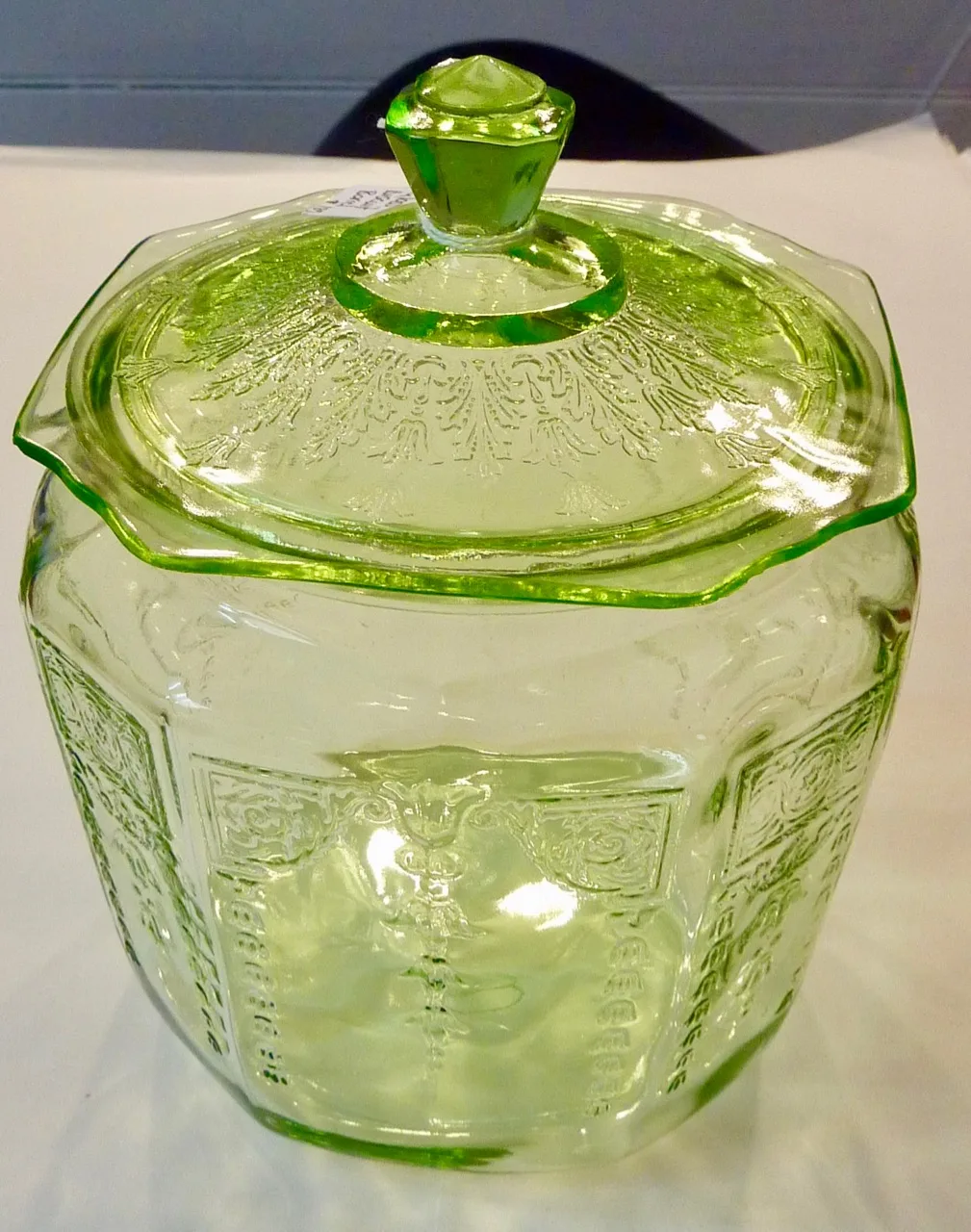 Green glass covered biscuit jar with panelled sides, moulded scroll-and-urn panels and a faceted knob on the lid