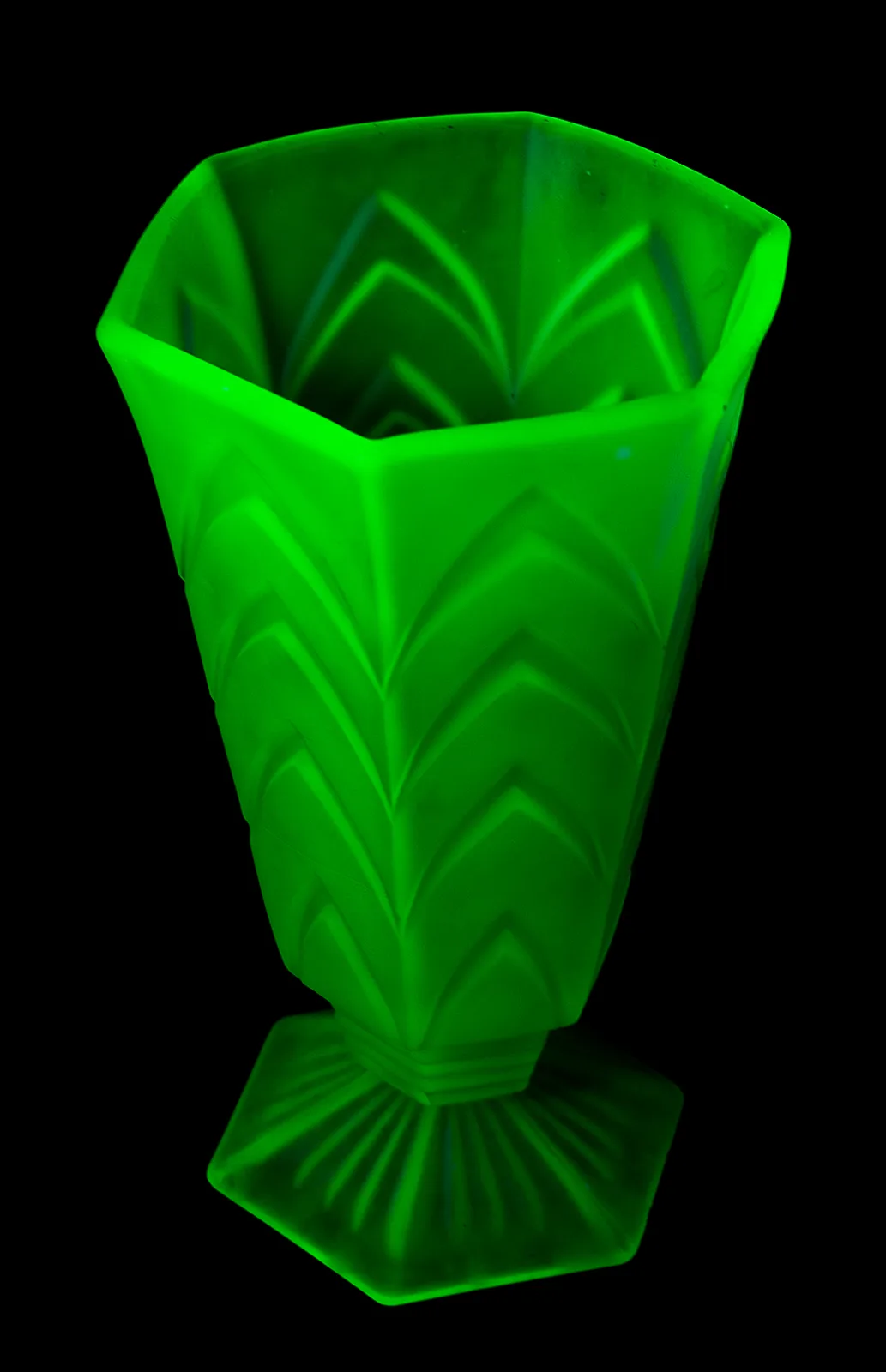 Faceted glass vase glowing brilliant green against a black background under ultraviolet light
