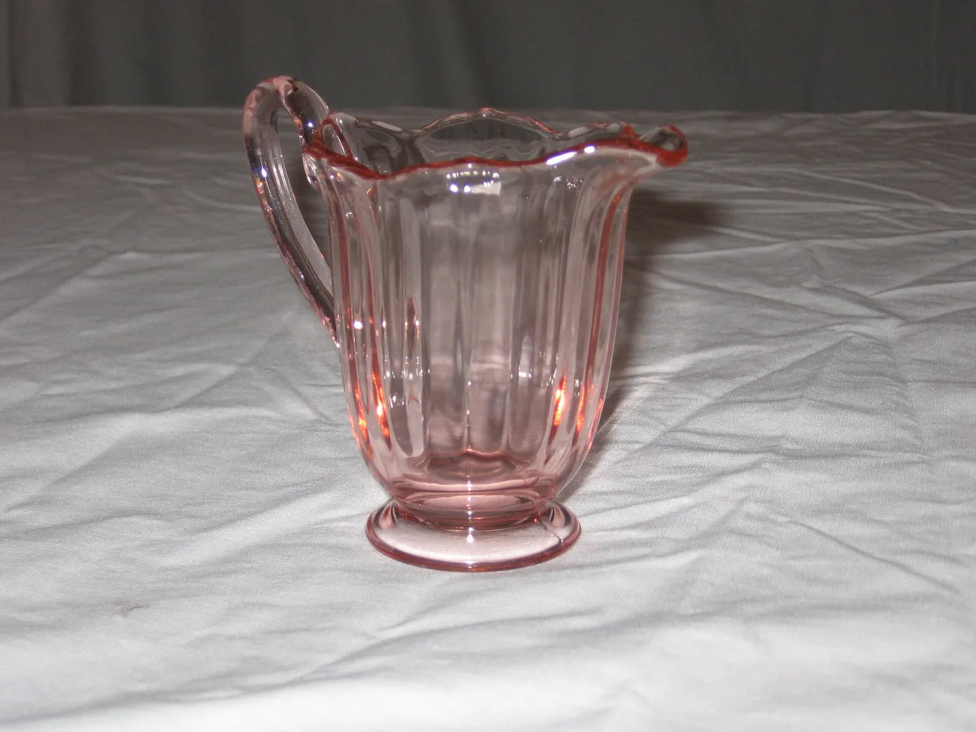 Pale pink pressed glass creamer with vertical panels, a pulled spout and a plain foot