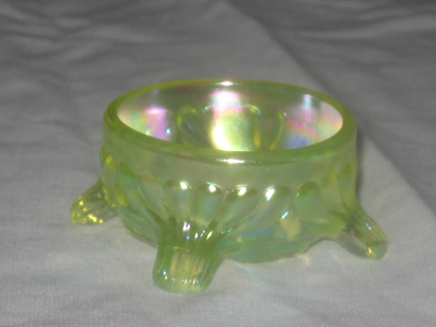 Small three-footed bowl in pale yellow-green glass with a rainbow sheen across its surface