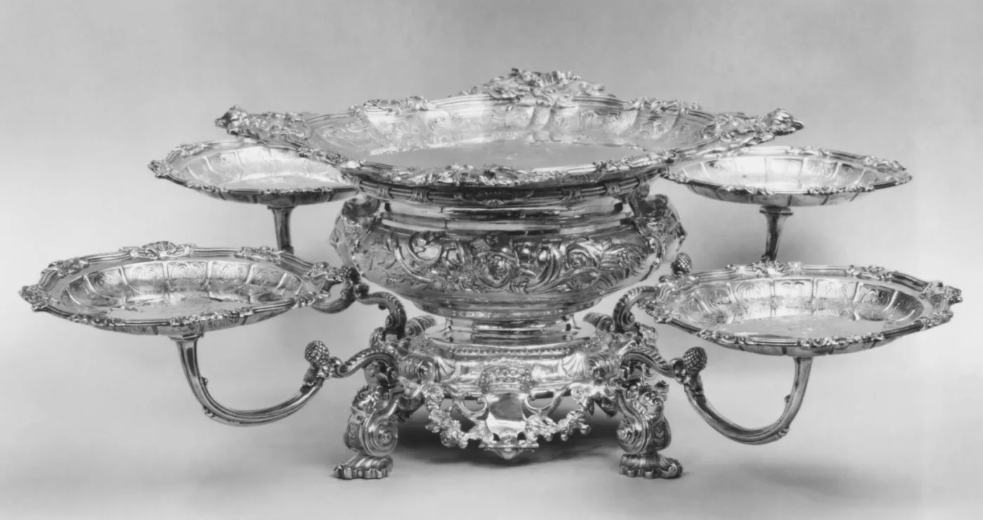 Low silver epergne with a shallow central bowl on a moulded stem, four scrolled arms radiating from it each supporting a small shell-shaped dish, on four cast feet