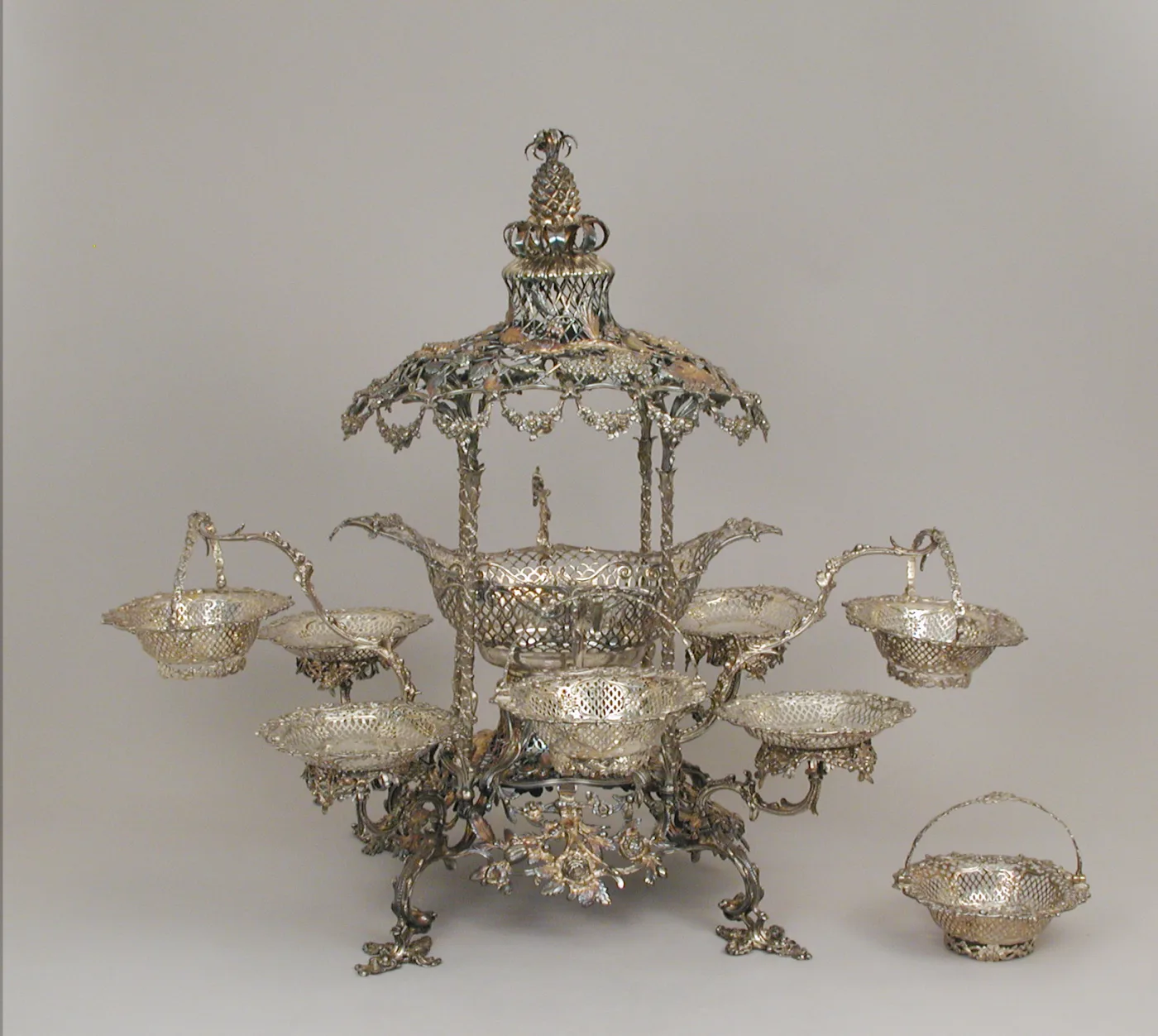 Elaborate silver centrepiece with a domed pierced canopy on scrolled supports over a central pierced basket, six smaller baskets hung and set on curving branches around it, standing on four cast scroll feet