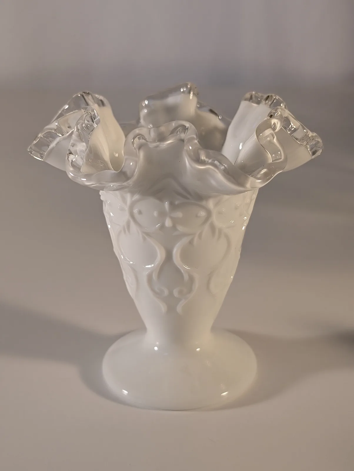 Milk-glass vase moulded with a raised scrolling lace pattern, finished with a tall clear crimped ruffle standing up around the rim