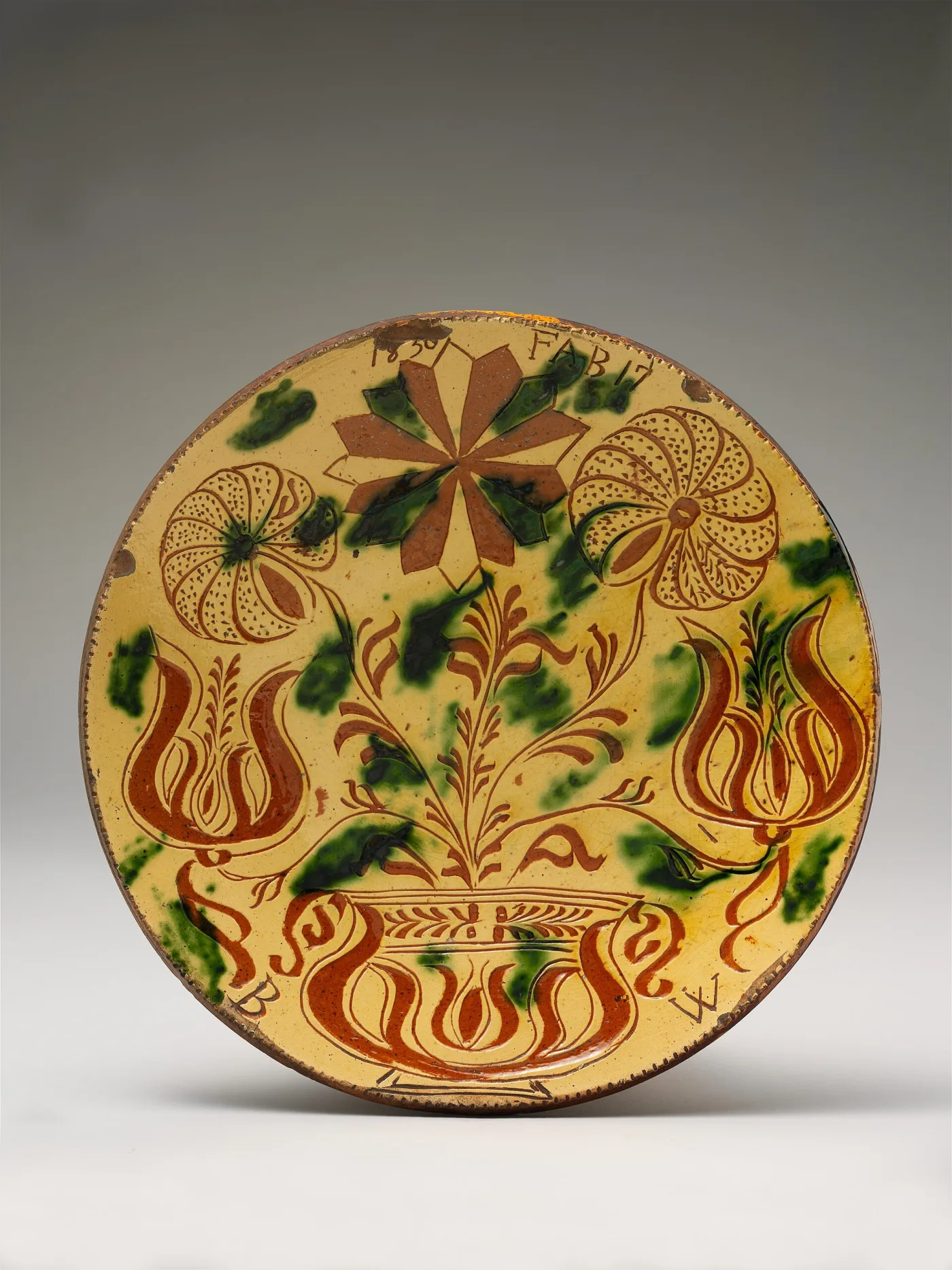 Yellow-slip earthenware plate with tulips, rosettes and a flowerpot incised through the slip in red-brown, with green splashes, dated 1830 at the rim