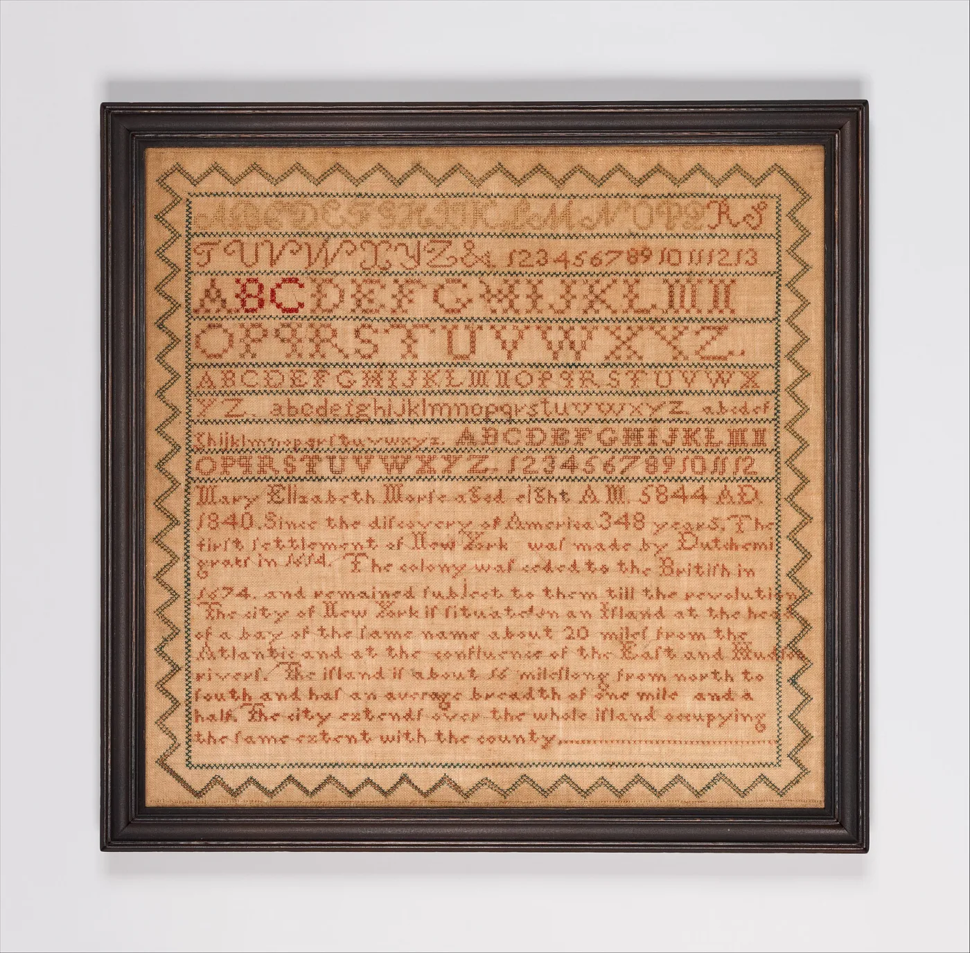 Sampler of 1840 in a black frame, worked almost entirely in red cross-stitch text with alphabets and a long passage about New York, inside a green zigzag border