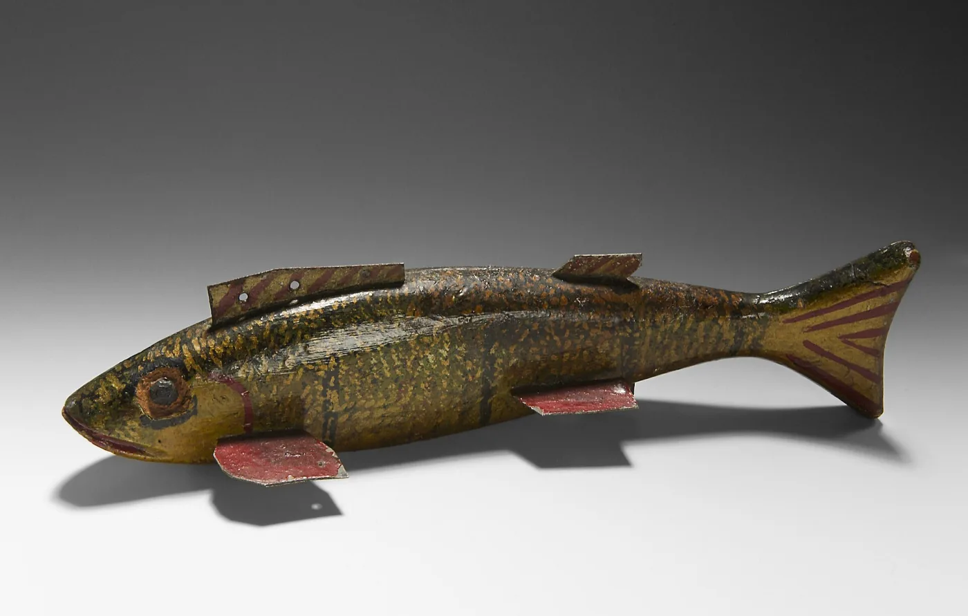 Carved wooden fish decoy painted olive and gold with red-striped tin fins and tail and a pierced metal plate on its back