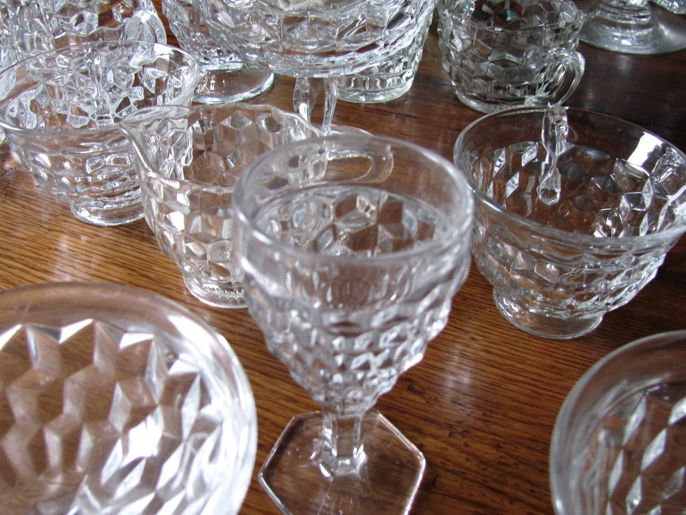 Group of heavy pressed glass cups, bowls and a stemmed goblet on a wooden table, all with a raised cubed block pattern and the goblet on a hexagonal foot