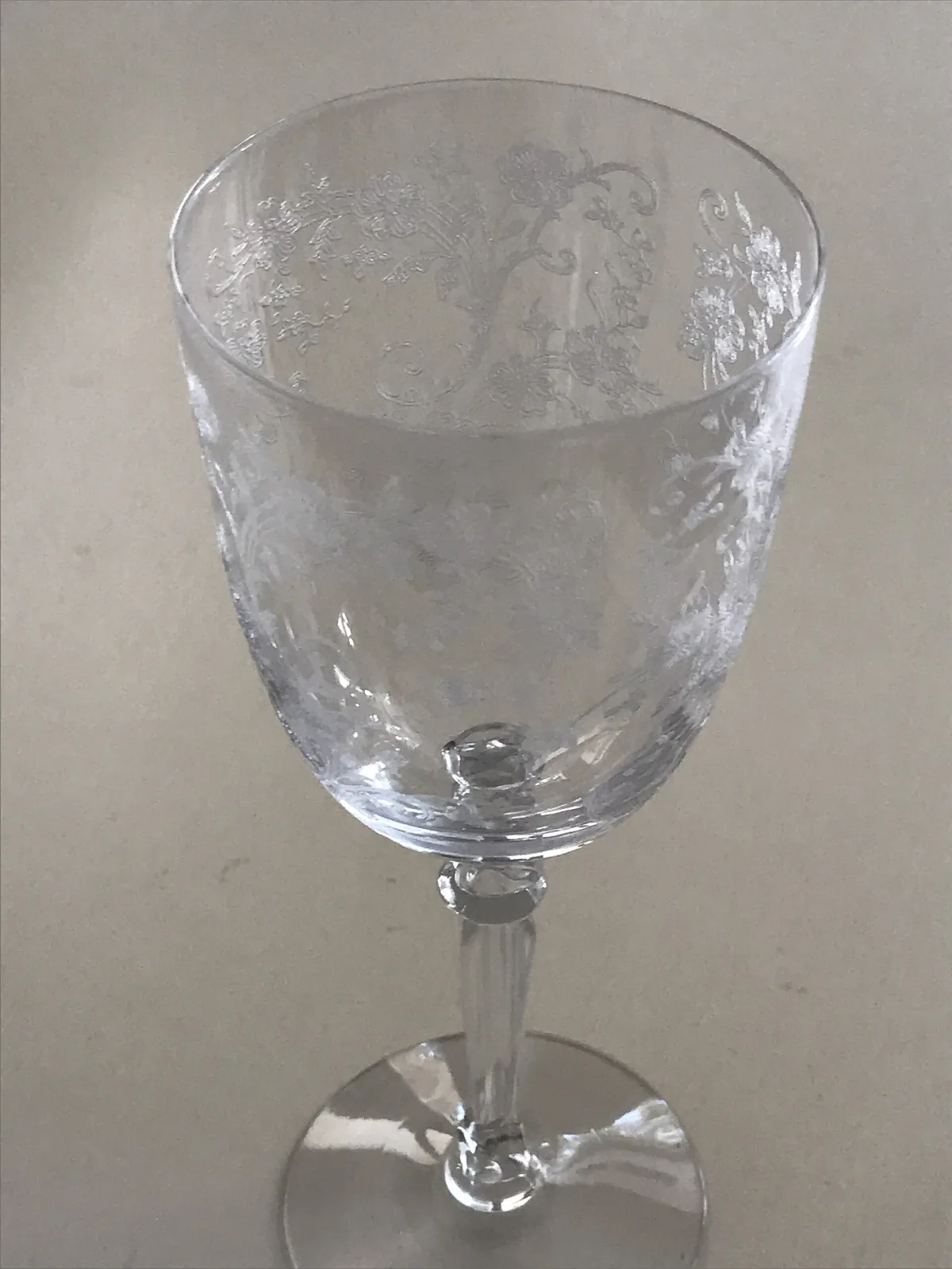 Close view of the upper bowl of an etched goblet, showing dense white floral and scroll ornament covering the glass, with a faceted knop below
