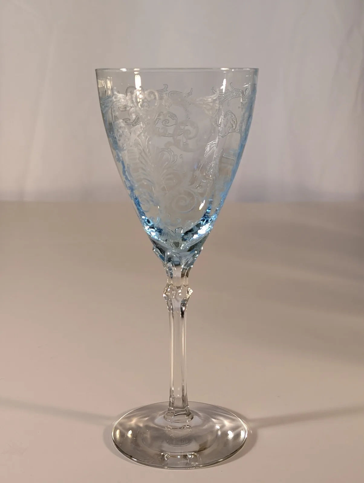 Wine goblet with a pale blue etched bowl carrying scrollwork and foliage, joined to a colourless faceted stem and foot
