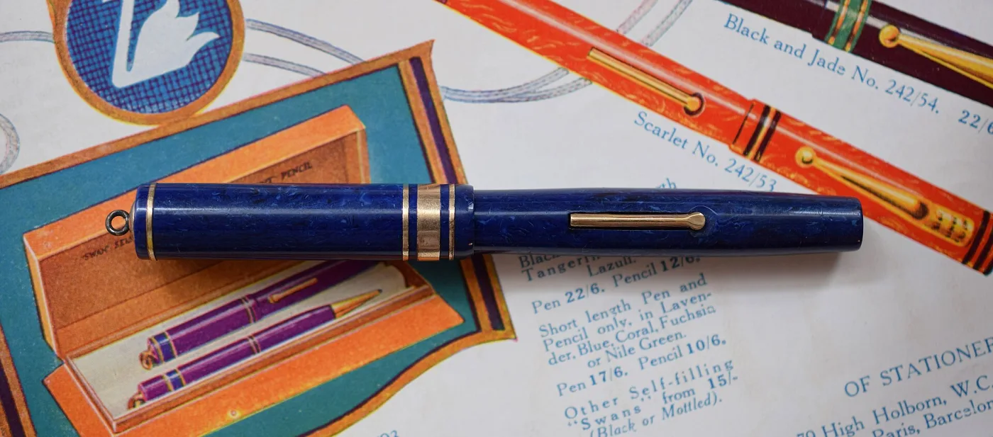 Blue and black marbled fountain pen with a gold clip and band, lying across sheets of printed period stationery advertising and price lists