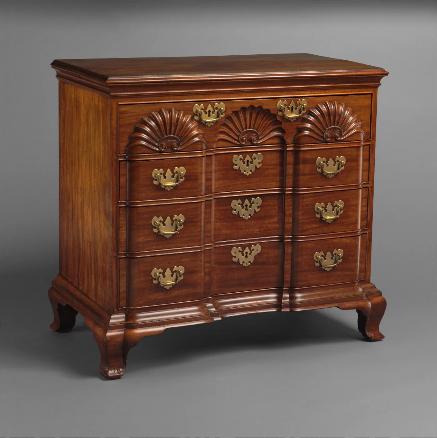 Mahogany block-front chest of drawers with three carved shells across the top drawer, brass bat-wing pulls and ogee bracket feet