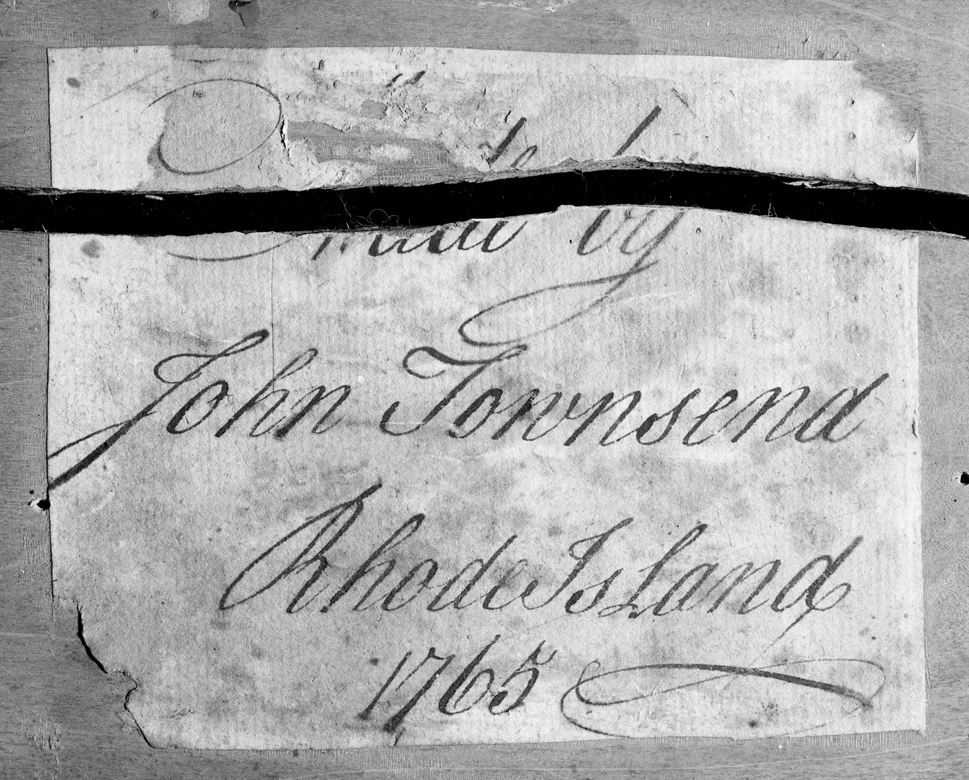 Torn handwritten paper label in copperplate script reading Made by John Townsend, Rhode Island, 1765, with a dark strip across its upper part