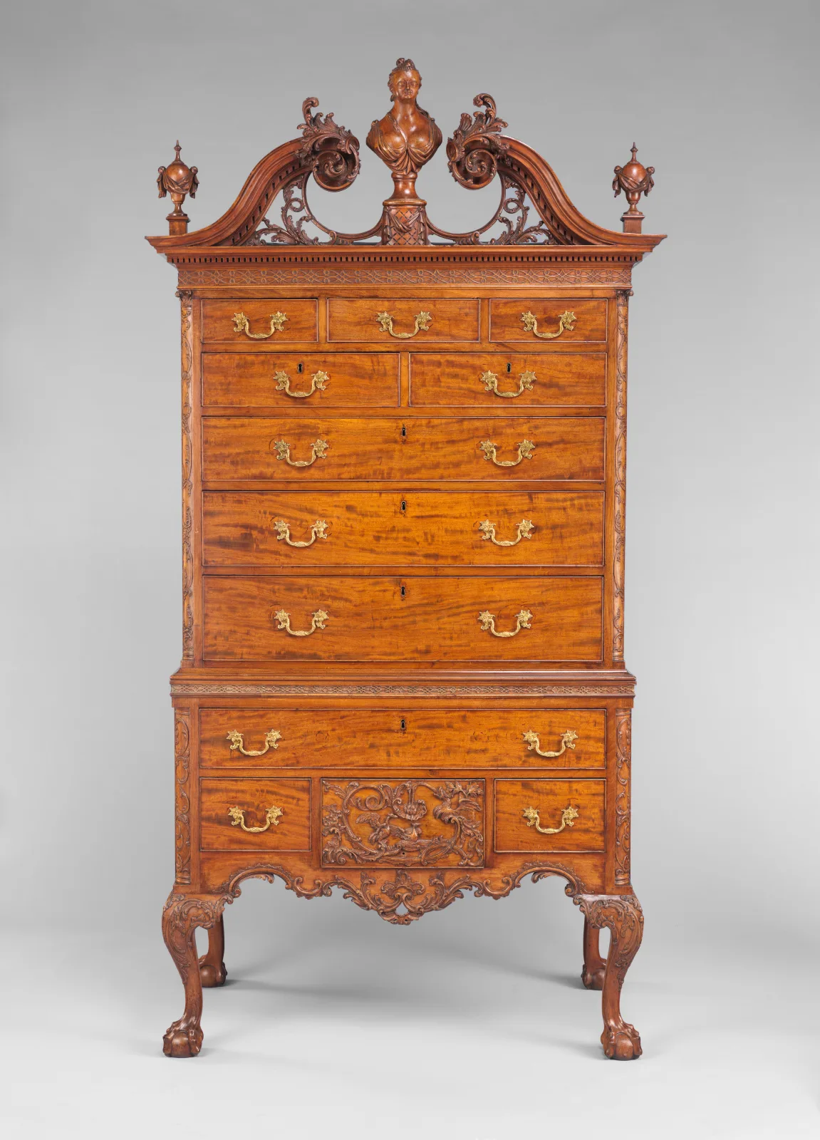 Tall mahogany high chest of drawers with a carved scroll pediment, flame finials, brass pulls and cabriole legs ending in claw-and-ball feet