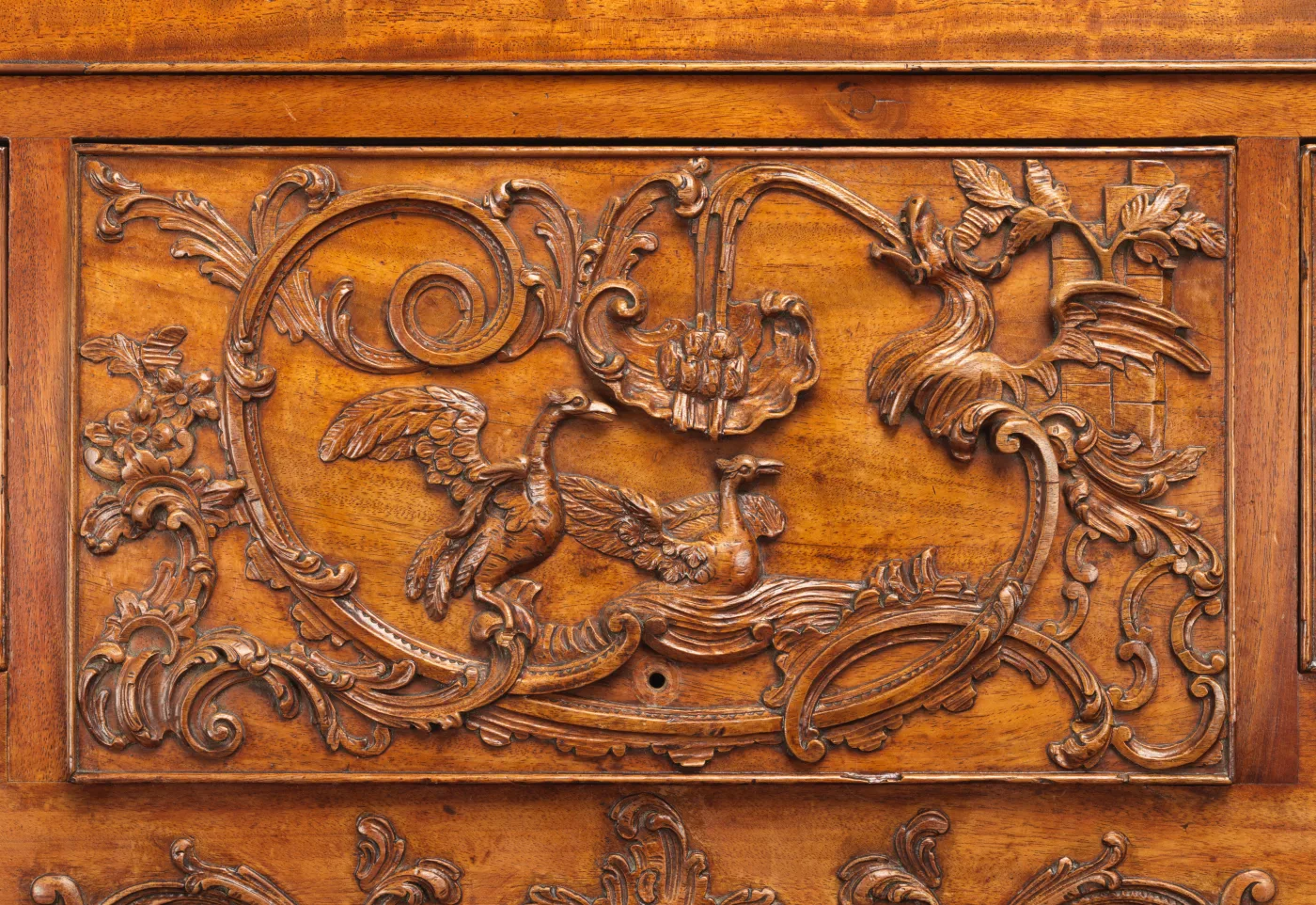 Carved mahogany drawer front with an asymmetrical rococo scroll, leaves and a bird, the carving darker in its recesses than on the high points