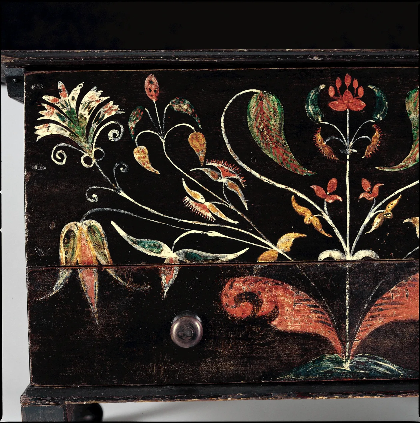Detail of a dark painted chest front decorated with stylised tulips, leaves and vines in red, white and yellow paint around a wooden knob