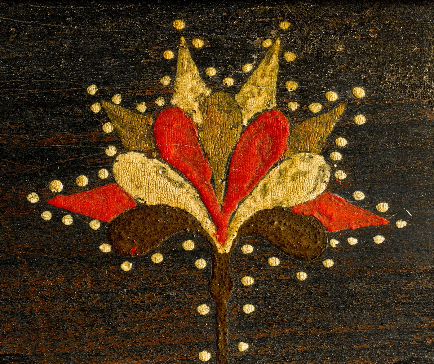 Close detail of a painted tulip in red and cream with a dotted yellow outline on a dark painted ground, the paint showing the texture of the wood beneath