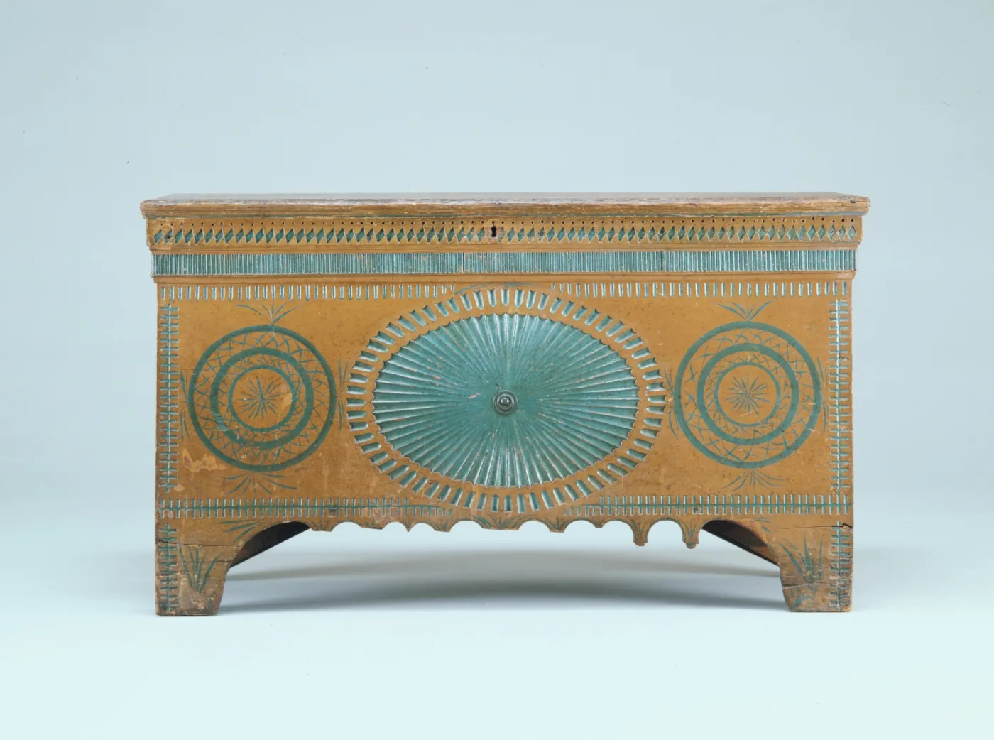 Pine chest painted ochre with a fluted oval and two rosettes outlined in green paint, and a scalloped skirt